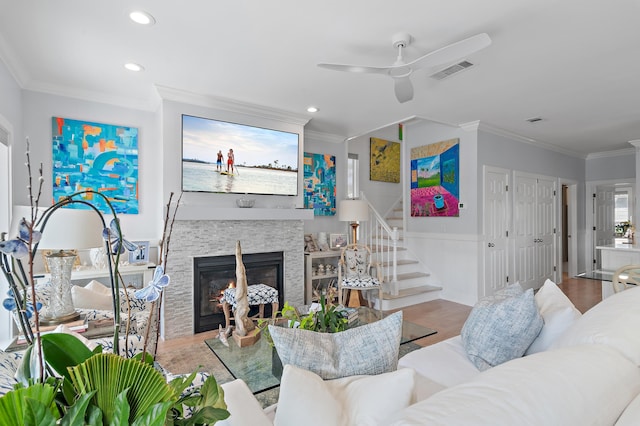 living area with visible vents, ornamental molding, wood finished floors, stairs, and a fireplace