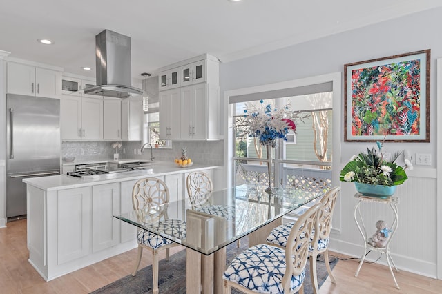 kitchen featuring island range hood, white cabinets, light countertops, appliances with stainless steel finishes, and tasteful backsplash