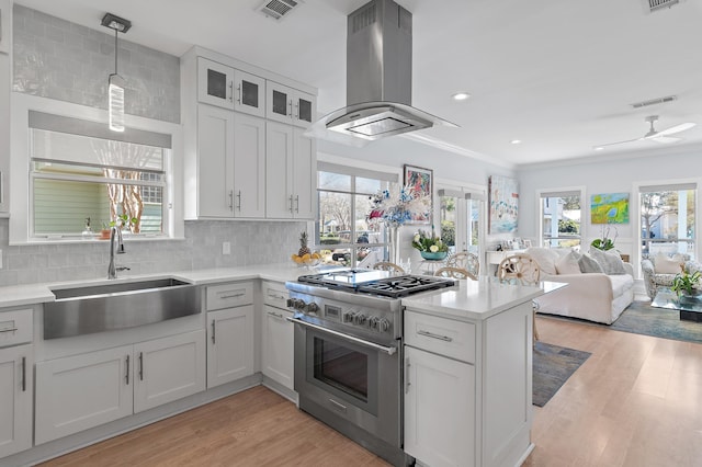 kitchen featuring stainless steel range, island exhaust hood, light countertops, visible vents, and a sink