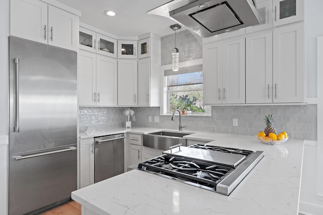 kitchen with a sink, white cabinets, range hood, appliances with stainless steel finishes, and light stone countertops