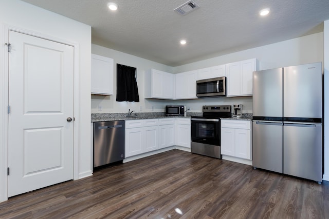 kitchen with light stone counters, visible vents, appliances with stainless steel finishes, dark wood-type flooring, and a sink