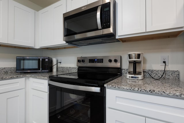 kitchen featuring stainless steel appliances, light stone counters, and white cabinetry