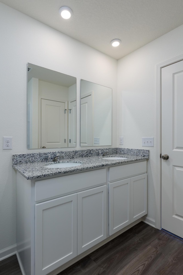 bathroom featuring double vanity, baseboards, a sink, and wood finished floors