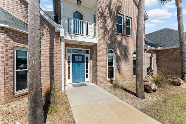 property entrance featuring roof with shingles, brick siding, and a balcony