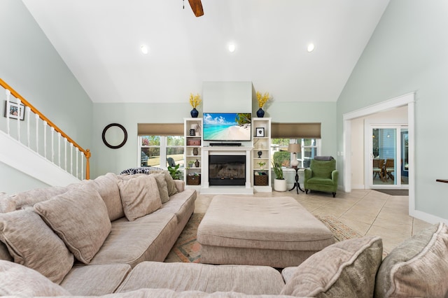 living room featuring high vaulted ceiling, plenty of natural light, a glass covered fireplace, and tile patterned floors