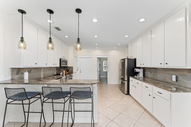 kitchen featuring light tile patterned floors, visible vents, appliances with stainless steel finishes, white cabinetry, and a kitchen breakfast bar