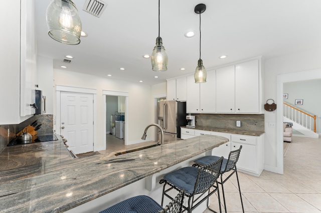 kitchen with light tile patterned floors, high quality fridge, a breakfast bar area, a sink, and visible vents