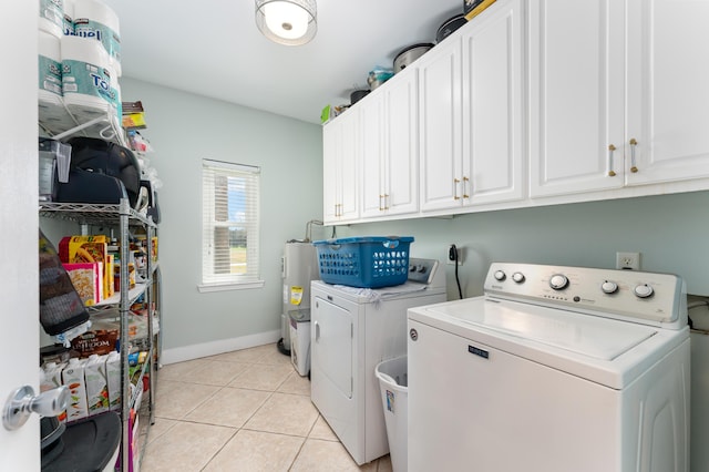 washroom featuring cabinet space, light tile patterned floors, baseboards, washing machine and clothes dryer, and water heater