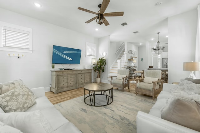 living room featuring visible vents, recessed lighting, stairs, ceiling fan with notable chandelier, and light wood-type flooring