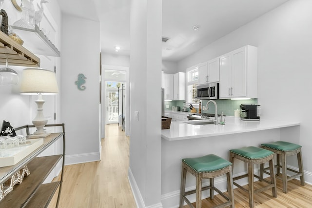 kitchen featuring stainless steel microwave, decorative backsplash, a kitchen breakfast bar, white cabinetry, and a sink