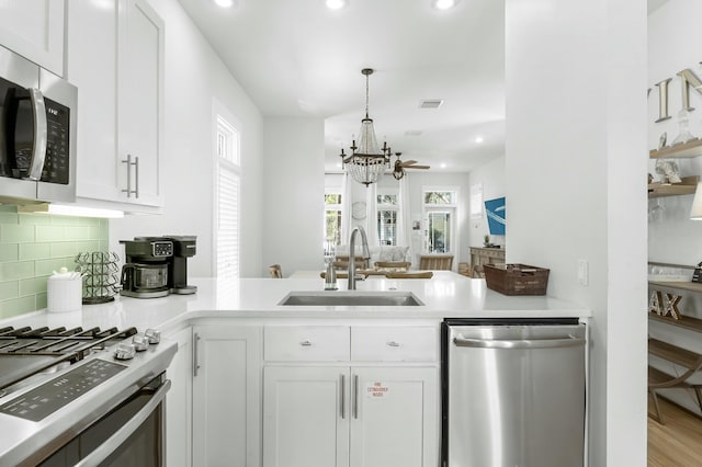 kitchen featuring visible vents, a sink, tasteful backsplash, appliances with stainless steel finishes, and a peninsula