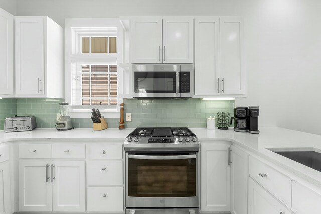 kitchen with decorative backsplash, white cabinets, appliances with stainless steel finishes, and light countertops