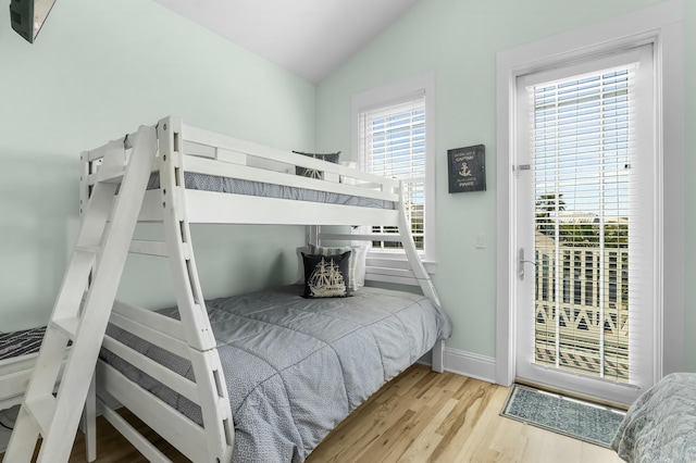 bedroom with access to outside, vaulted ceiling, baseboards, and wood finished floors