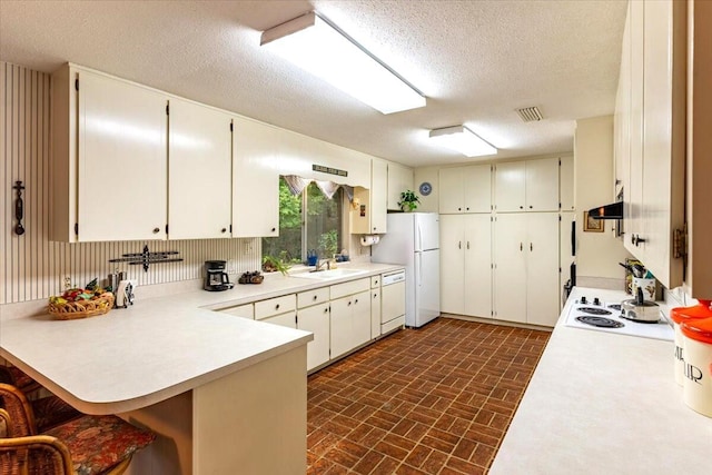 kitchen with brick patterned floor, a sink, a peninsula, white appliances, and under cabinet range hood