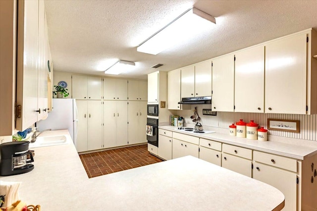 kitchen with brick floor, under cabinet range hood, light countertops, black appliances, and a sink