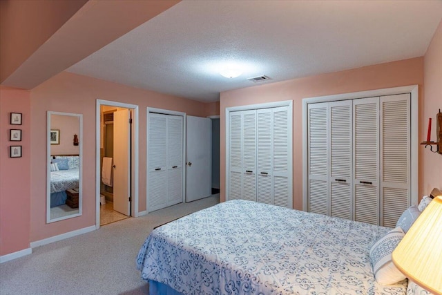 carpeted bedroom with visible vents, baseboards, and two closets