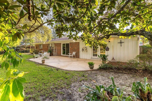 back of house with brick siding, a patio, and a lawn