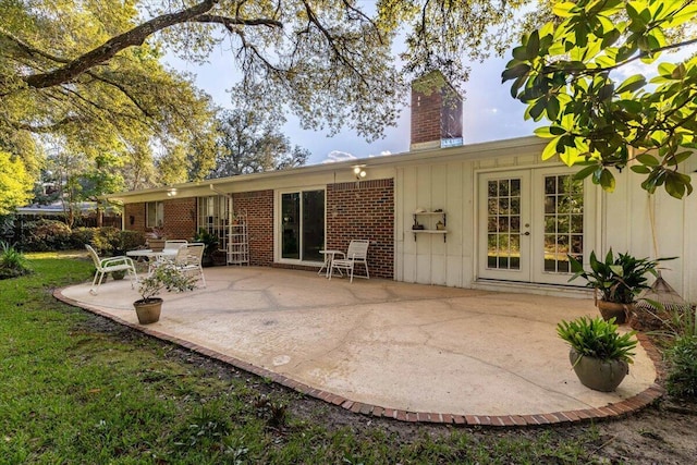 back of property featuring a patio, brick siding, french doors, board and batten siding, and a chimney