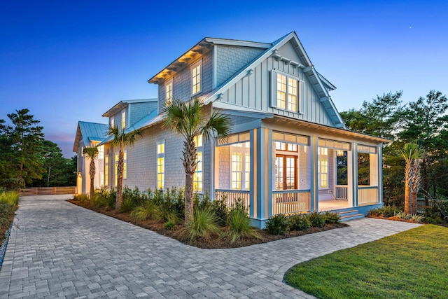 exterior space featuring a porch, a lawn, decorative driveway, board and batten siding, and a standing seam roof