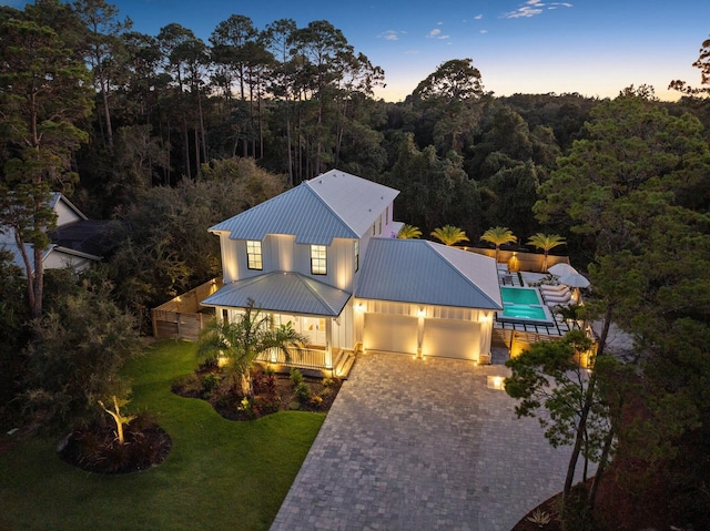 view of front of house featuring decorative driveway, a front yard, a standing seam roof, metal roof, and a wooded view