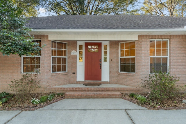 property entrance featuring brick siding, covered porch, and roof with shingles