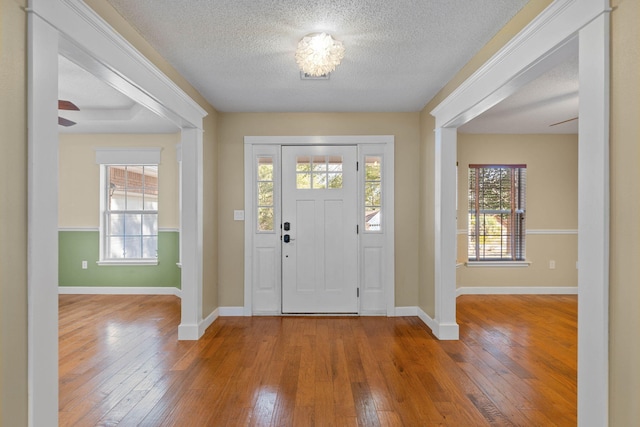 foyer entrance with a textured ceiling, baseboards, and wood-type flooring