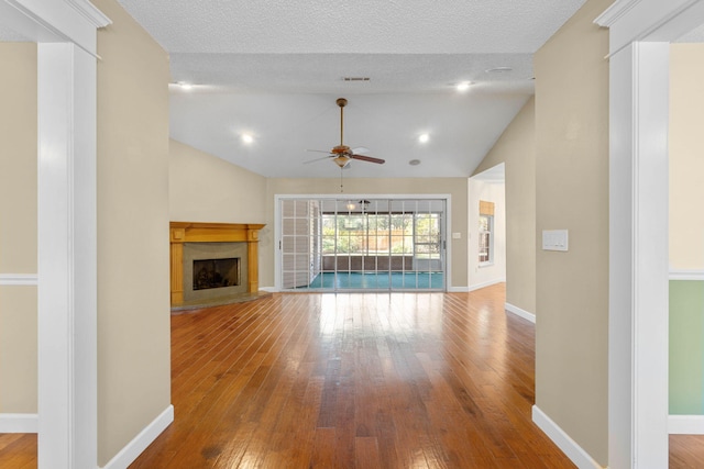 unfurnished living room featuring a fireplace with raised hearth, hardwood / wood-style flooring, baseboards, and vaulted ceiling