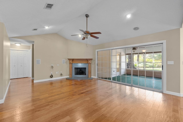 unfurnished living room featuring vaulted ceiling, a fireplace with raised hearth, light wood-style floors, and visible vents