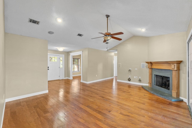 unfurnished living room featuring visible vents, a fireplace with raised hearth, light wood-style flooring, and vaulted ceiling