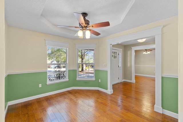 empty room with a tray ceiling, baseboards, wood-type flooring, and a textured ceiling