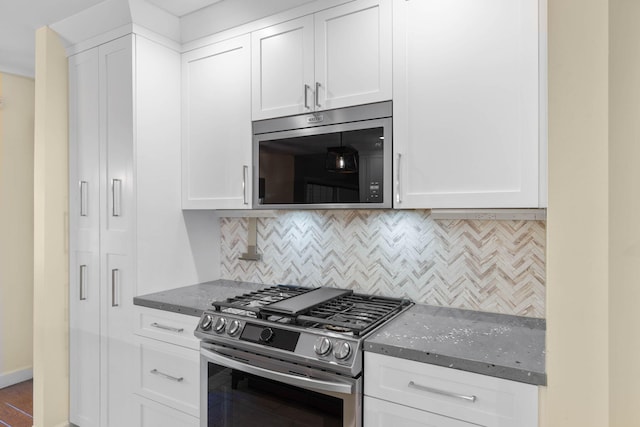 kitchen with stainless steel appliances, backsplash, white cabinets, and dark stone counters