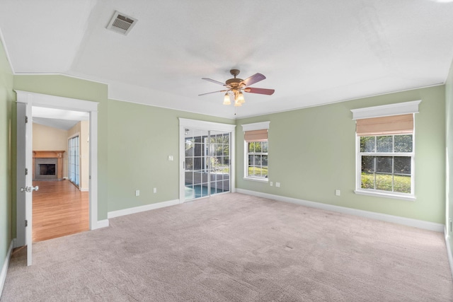 carpeted empty room featuring visible vents, ceiling fan, baseboards, lofted ceiling, and a fireplace