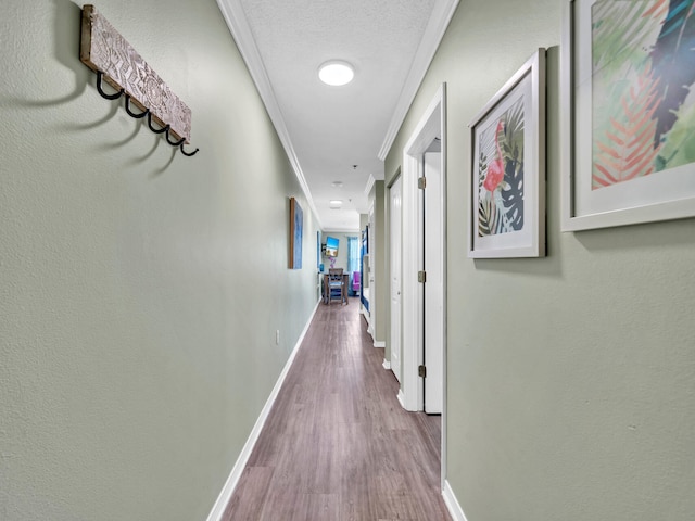 corridor featuring baseboards, a textured ceiling, wood finished floors, and crown molding