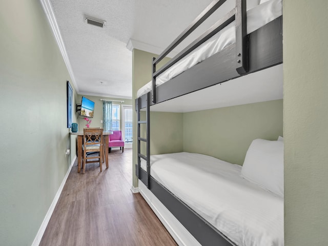 bedroom featuring crown molding, visible vents, a textured ceiling, wood finished floors, and baseboards