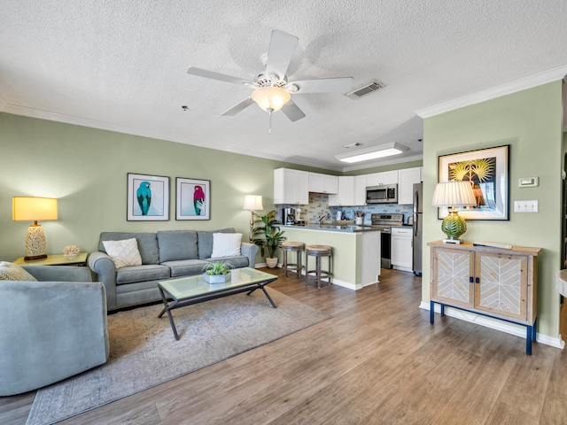 living room featuring visible vents, ceiling fan, ornamental molding, wood finished floors, and a textured ceiling