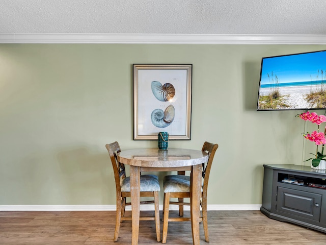 dining area featuring crown molding, a textured ceiling, baseboards, and wood finished floors