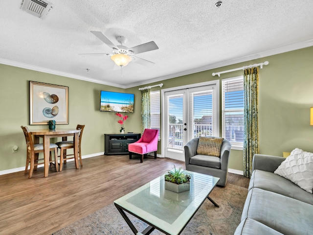 living room with wood finished floors, visible vents, baseboards, french doors, and crown molding