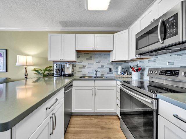 kitchen featuring stainless steel appliances, a peninsula, a sink, ornamental molding, and light wood finished floors