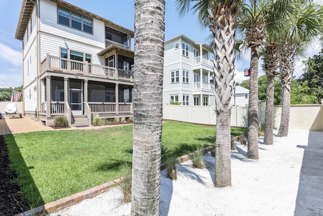 back of house with a balcony, fence, a yard, and a sunroom