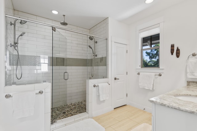 bathroom with wood finished floors, recessed lighting, a shower stall, baseboards, and vanity