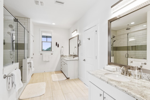 bathroom featuring visible vents, a shower stall, baseboards, two vanities, and a sink