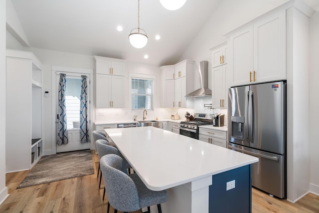 kitchen featuring a kitchen island, stainless steel appliances, vaulted ceiling, wall chimney range hood, and backsplash