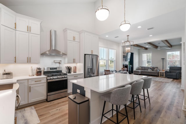 kitchen with a kitchen island, wall chimney range hood, light countertops, light wood-style flooring, and stainless steel appliances