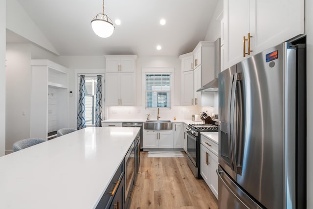 kitchen featuring a sink, white cabinets, appliances with stainless steel finishes, wall chimney exhaust hood, and backsplash