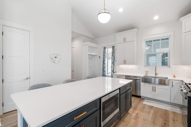 kitchen with light countertops, vaulted ceiling, appliances with stainless steel finishes, white cabinets, and a sink