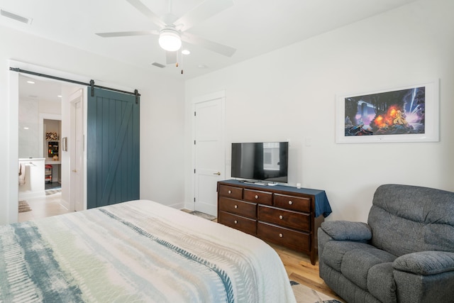 bedroom featuring light wood finished floors, visible vents, ceiling fan, and a barn door