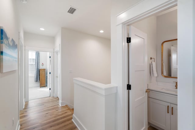 corridor featuring visible vents, light wood-style flooring, a sink, recessed lighting, and baseboards