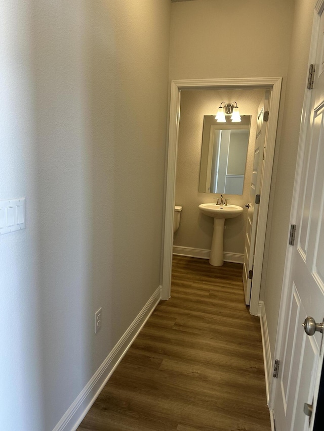 corridor with dark wood-type flooring, a sink, and baseboards