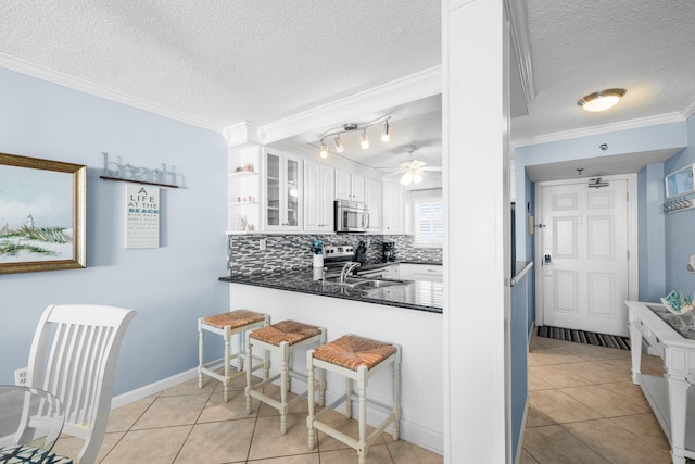 kitchen featuring white cabinetry, appliances with stainless steel finishes, dark countertops, glass insert cabinets, and crown molding