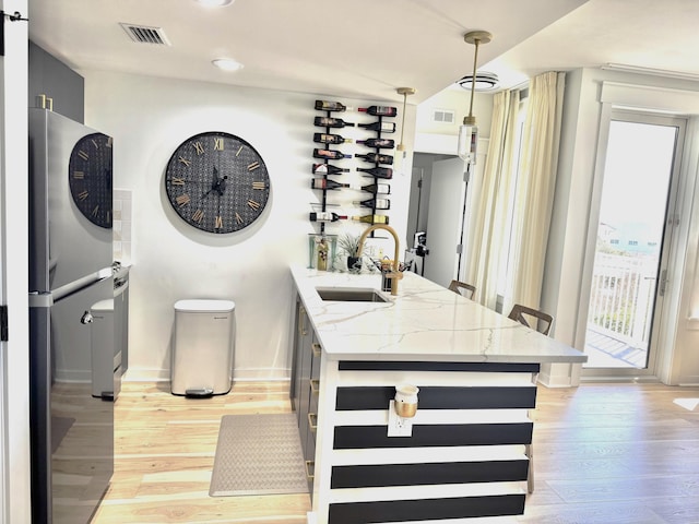 interior space with light wood-style flooring, visible vents, pendant lighting, and a sink